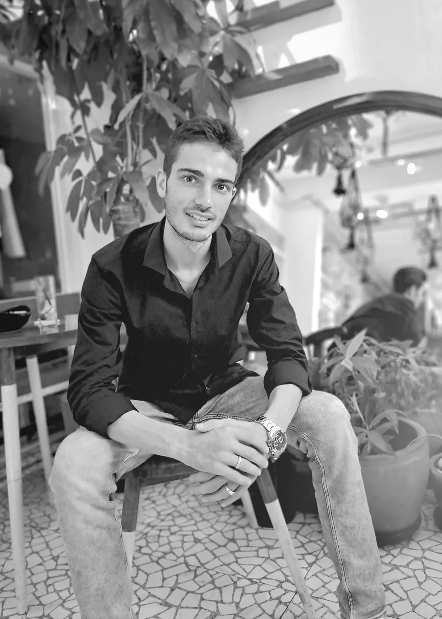 Sayid Bilal seated on a stool in a navy shirt, smiling to camera.