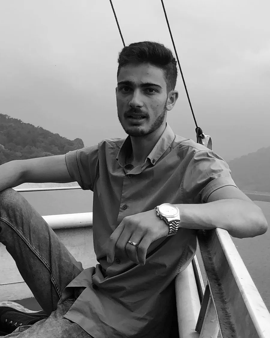 Sayid Bilal seated on a wooden deck above a lake, a mountain behind him.